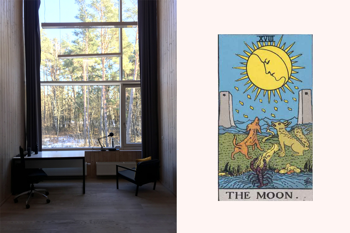 A desk and two chairs in front of a tall window, looking out into snow and pines, next to The Moon tarot card