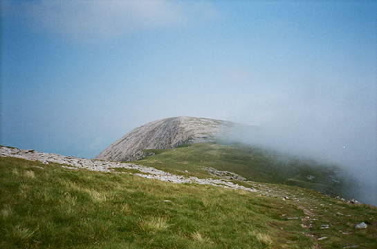 The top of a mountain in Wales, with low clouds wafting over the grass