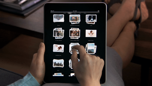 A person pinches a stack of photos on an iPad. When they spread their fingers apart, the album expands to a grid view.