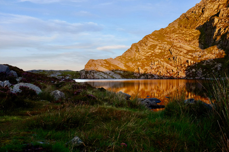 The same lake, closer. It's a bit darker now and the lake is reflecting the orange of the sunset and rocks above.