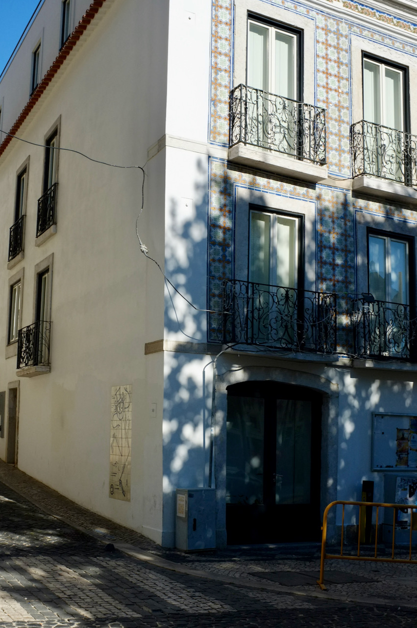 A corner in Lisbon's Anjos area. One wall is covered in the classic blue and white tiles, in dappled sunlight.