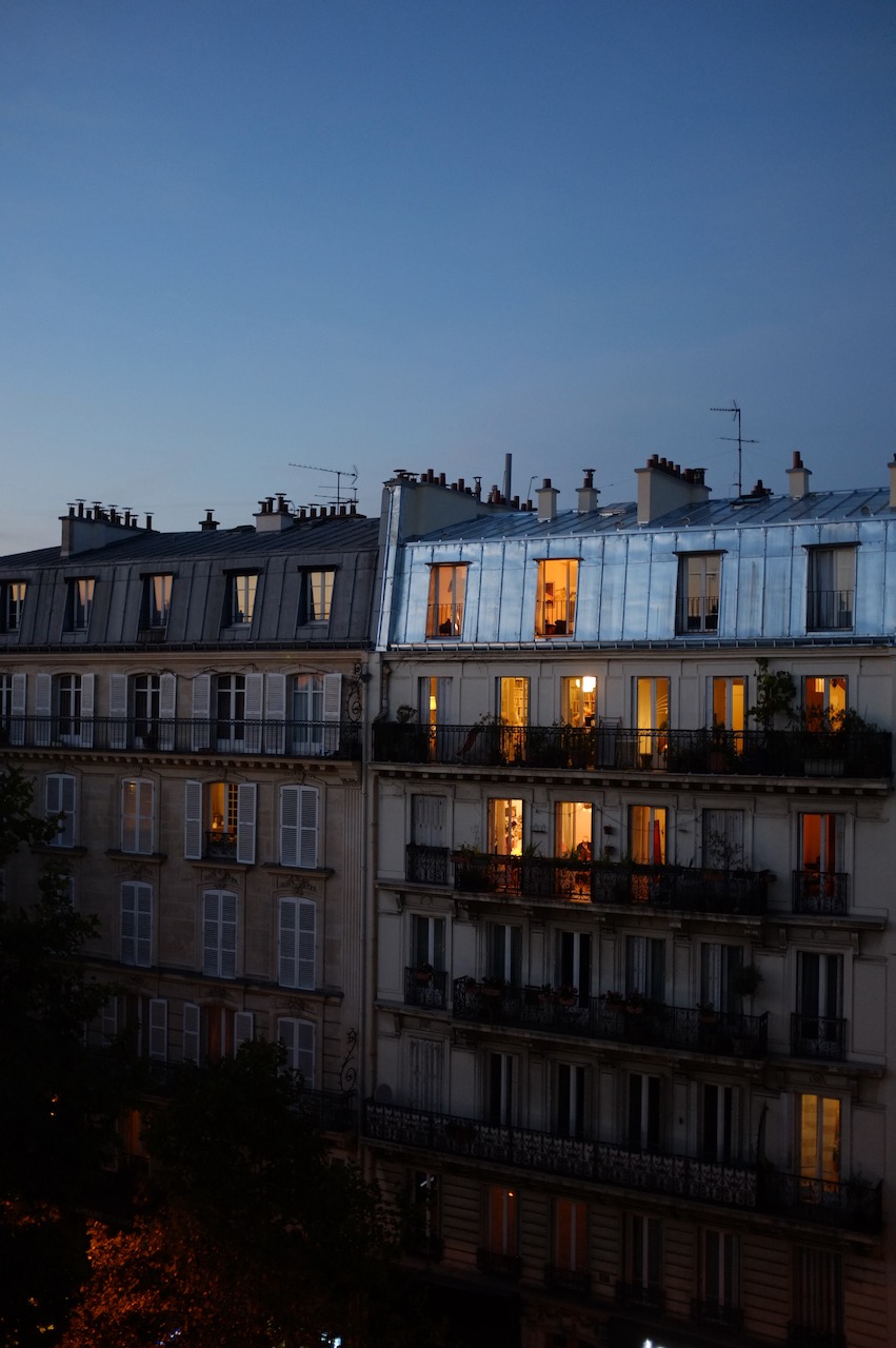Parisian apartment blocks at twilight. The lights are on and they look warm and cozy against the evening sky.