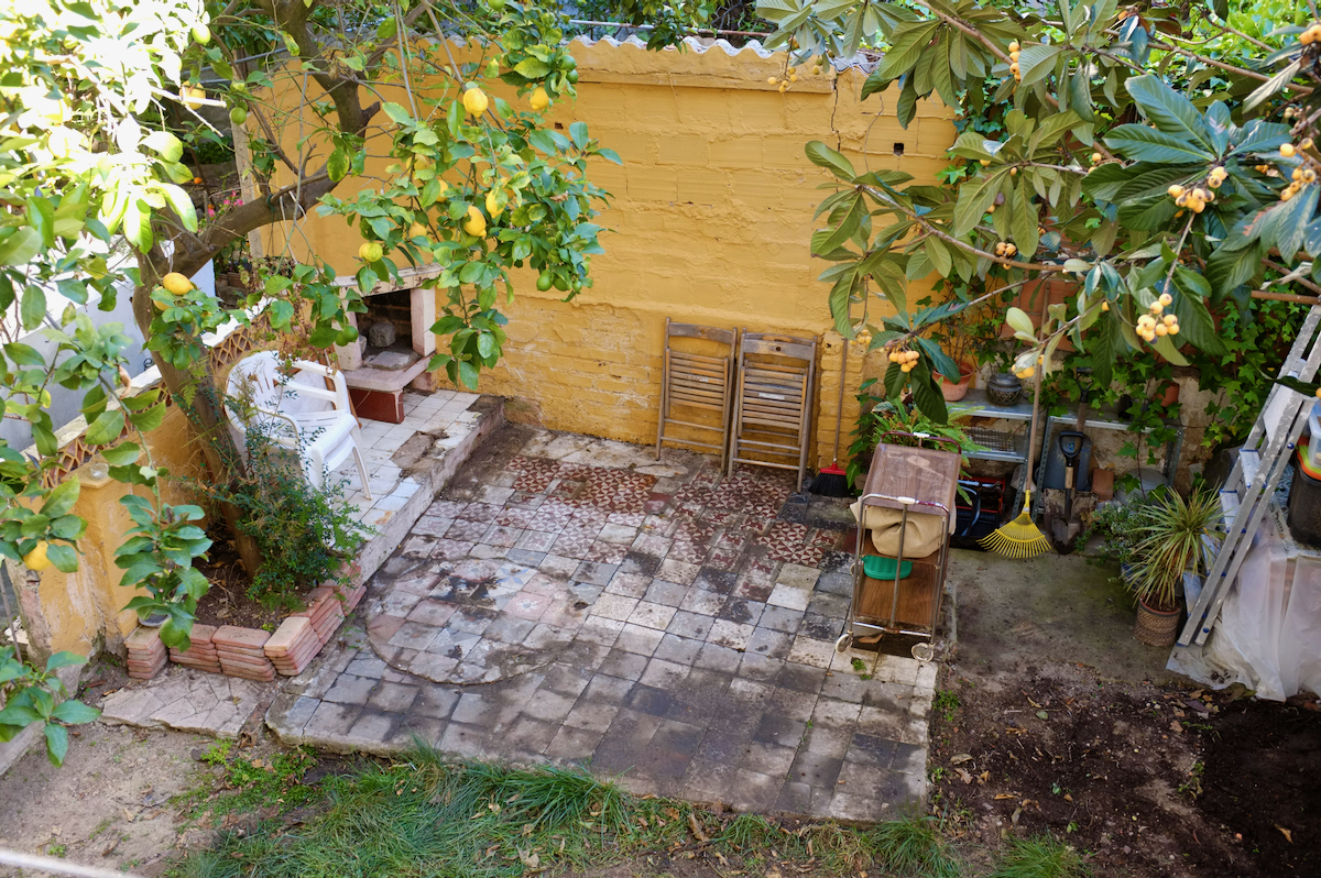 Our newly improved back garden with the lemon tree on the left and loquat on the right. The tiled area looks neat and freshly swept, with gardening tools on shelves in one corner.