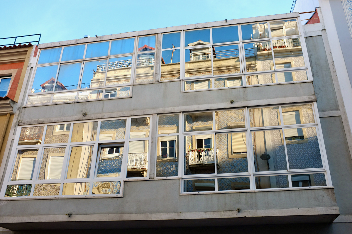 Mirrored apartment windows reflecting a tiled facade opposite.