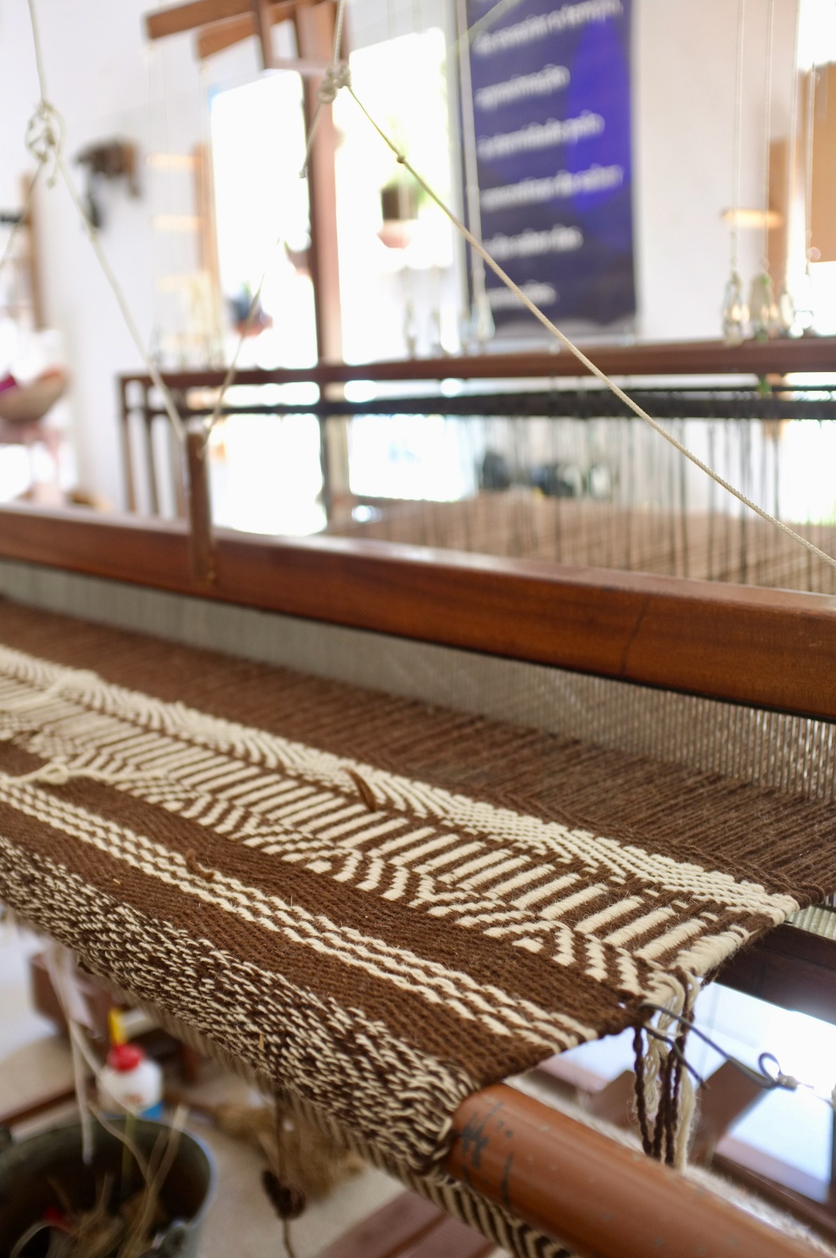 A wooden loom with a brown and cream patterned weaving on it.