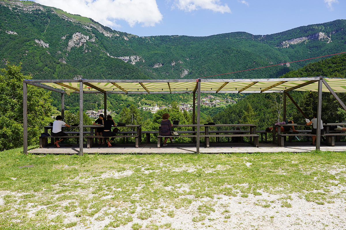 People sitting at the table at Il Masetto, reading. There is an incredible view across the valley to the next mountain, covered in forests