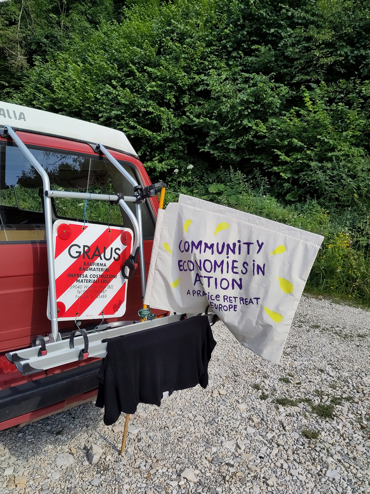 A campervan with a flag hanging off it that says "Community Economies in Action: A Practice Retreat in Europe."