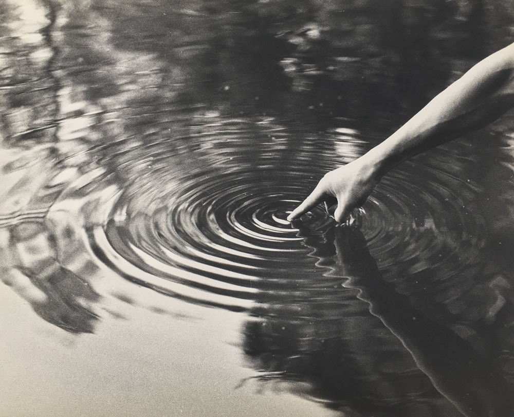 a photograph of a person touching water and concentric rings of a ripple go outward