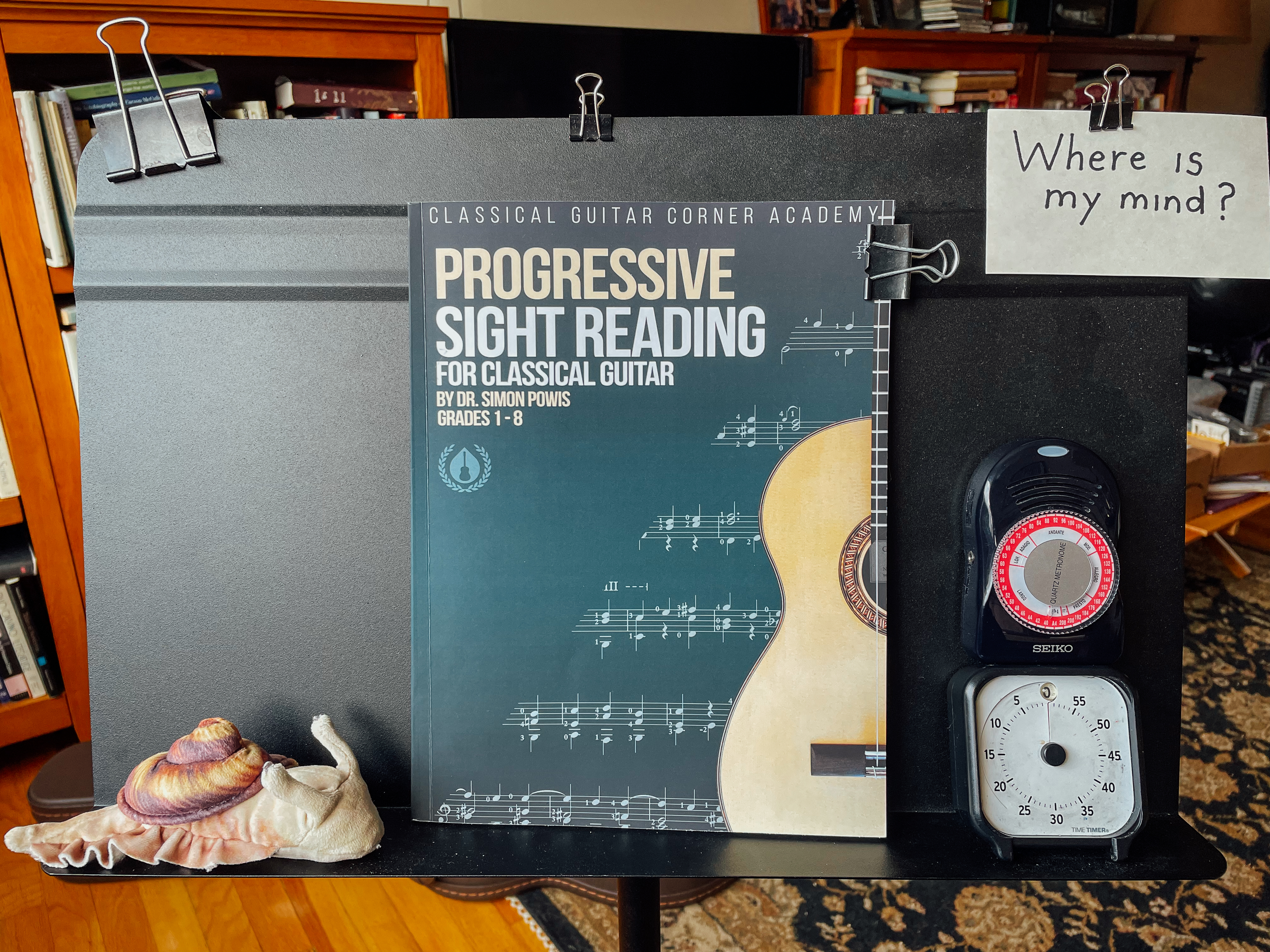 Music stand with sight reading book, plush snail, metronome, a timer, and index card that says “Where is my mind?”