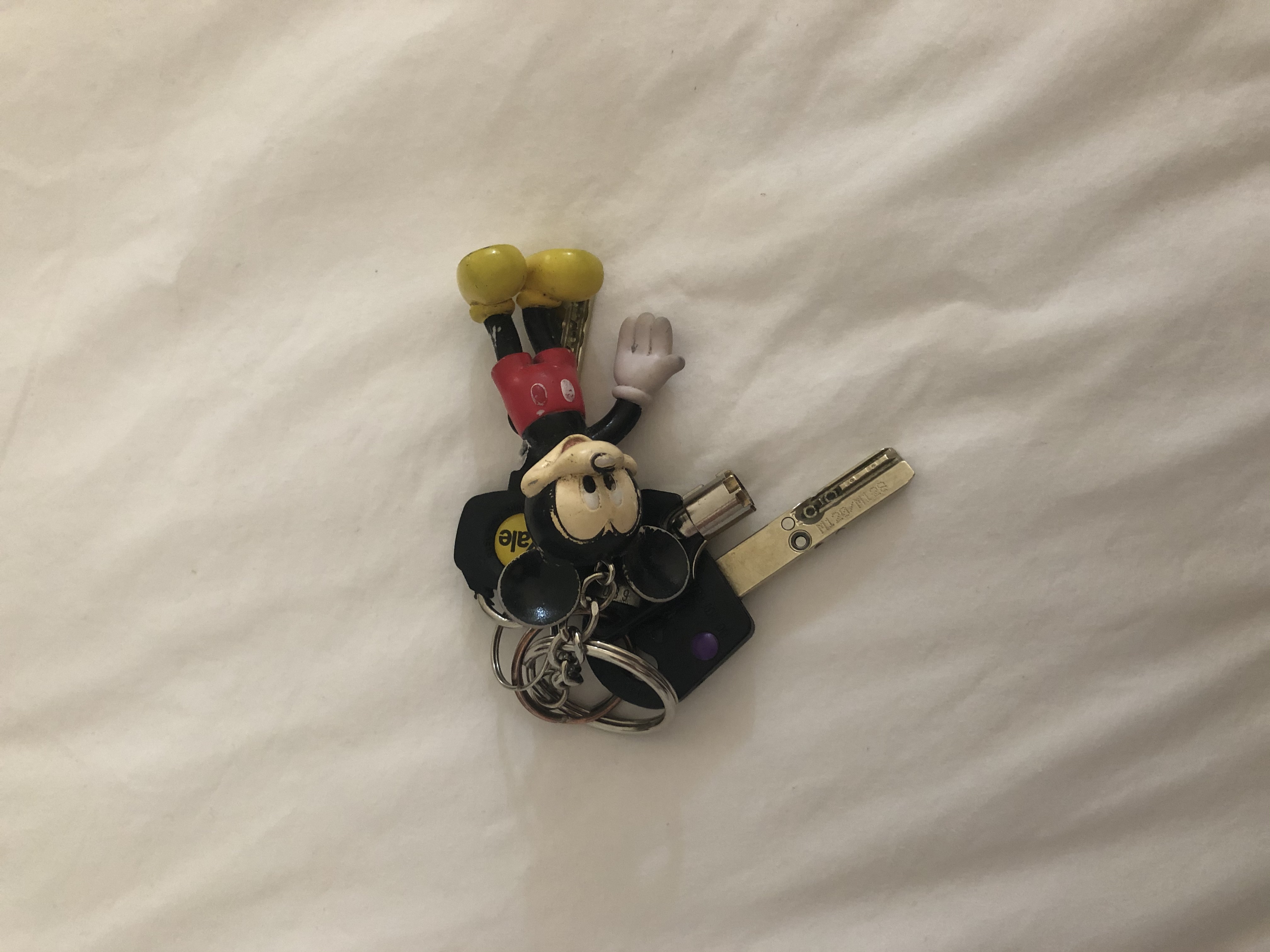a set of three keys and a mickey mouse keyring on a placed white sheet photographed from above